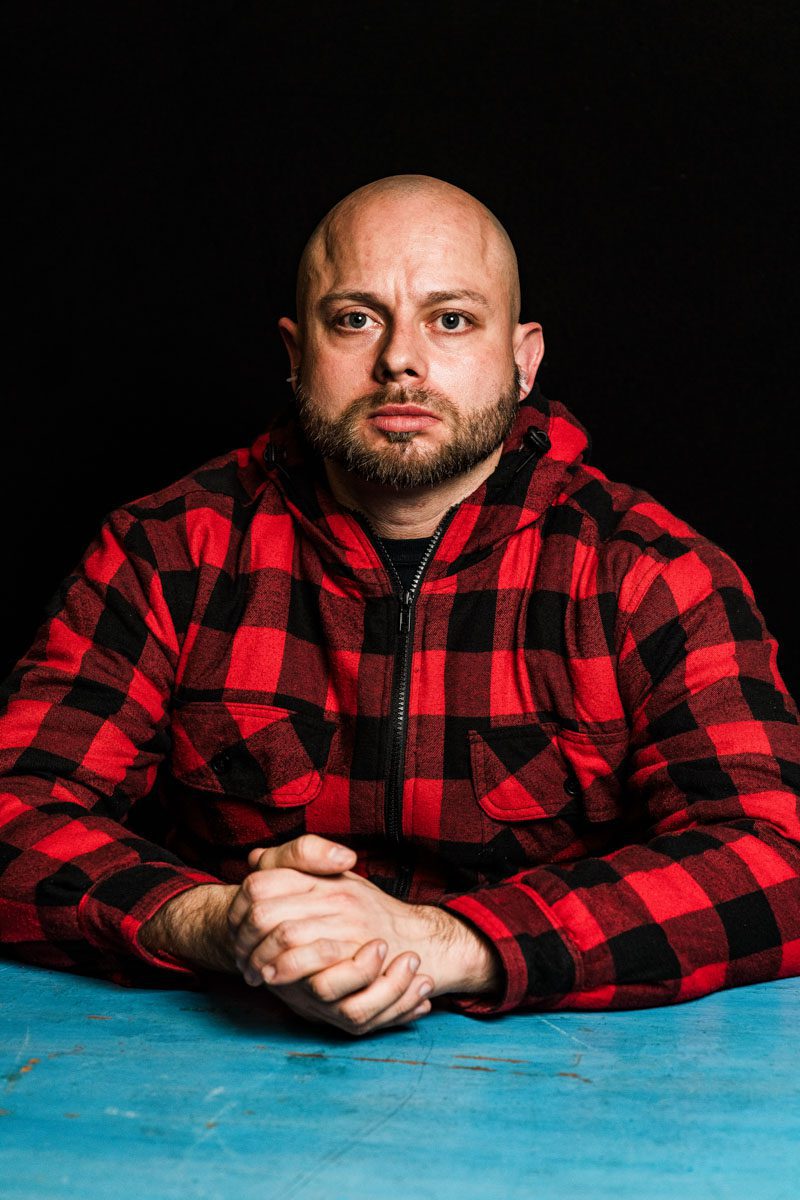 A metalhead with a short beard and no hair sitting at a table.