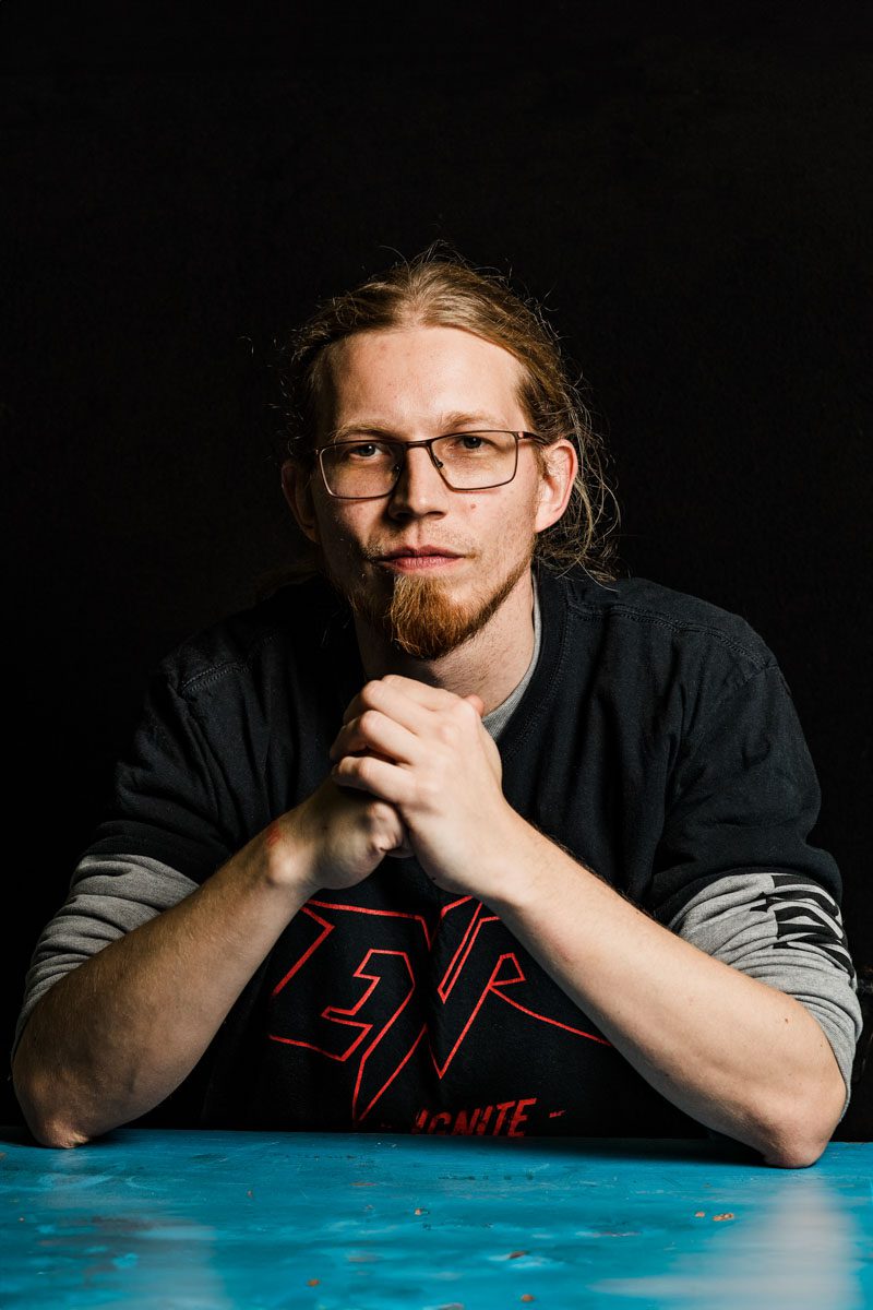 A metalhead with long hair and a goat beard sitting at a table.