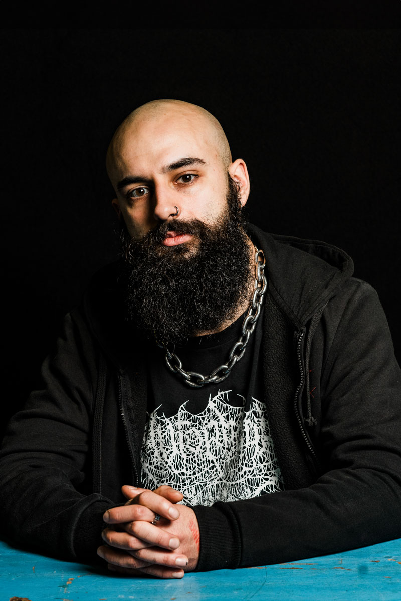 A metalhead with no hair and long beard sitting at a table.
